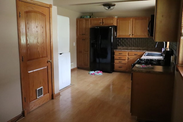 kitchen featuring stove, black fridge, sink, light hardwood / wood-style flooring, and decorative backsplash