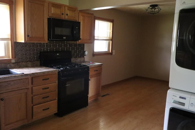 kitchen with black appliances, decorative backsplash, a healthy amount of sunlight, and stacked washer and clothes dryer