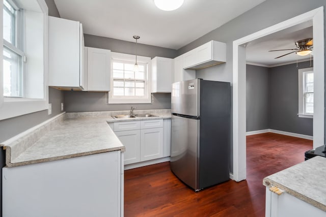 kitchen with a wealth of natural light, sink, white cabinets, stainless steel fridge, and hanging light fixtures