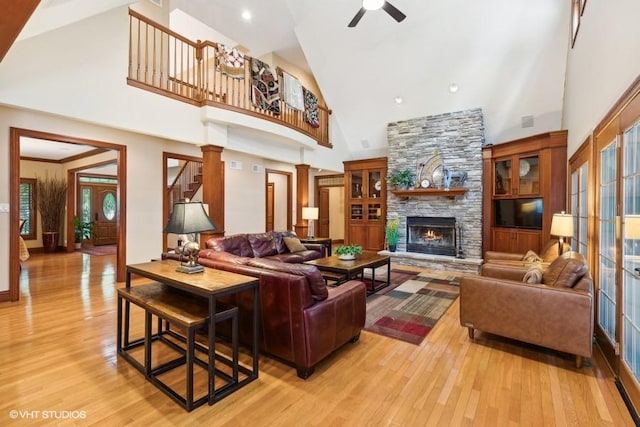 living room featuring ceiling fan, a stone fireplace, high vaulted ceiling, and light hardwood / wood-style flooring