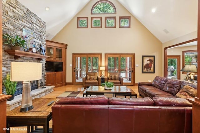 living room featuring a stone fireplace, a towering ceiling, and light wood-type flooring