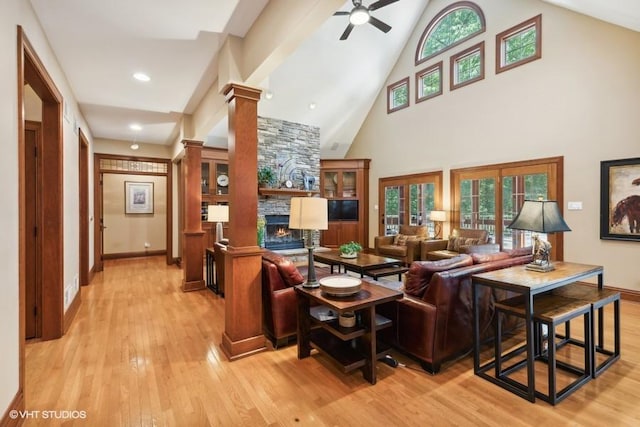 living room with ceiling fan, high vaulted ceiling, decorative columns, a stone fireplace, and light wood-type flooring