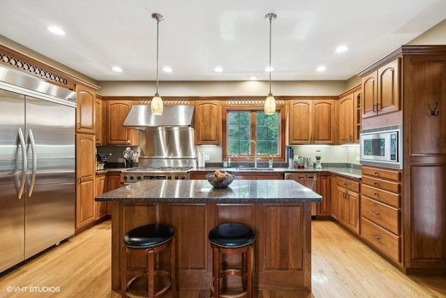 kitchen featuring built in appliances, light hardwood / wood-style flooring, a kitchen island, pendant lighting, and range hood