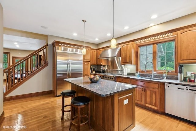 kitchen featuring sink, dark stone counters, built in refrigerator, white dishwasher, and wall chimney range hood