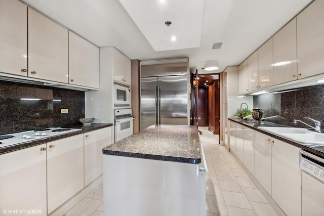 kitchen with tasteful backsplash, sink, built in appliances, white cabinets, and a center island