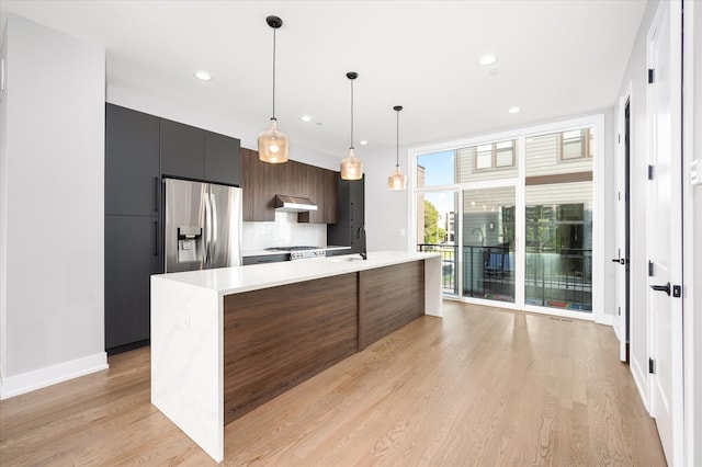 kitchen with backsplash, a kitchen island with sink, stainless steel fridge with ice dispenser, and light wood-type flooring