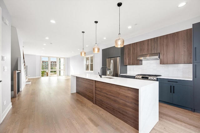 kitchen featuring a center island with sink, light wood-type flooring, stainless steel fridge with ice dispenser, and hanging light fixtures