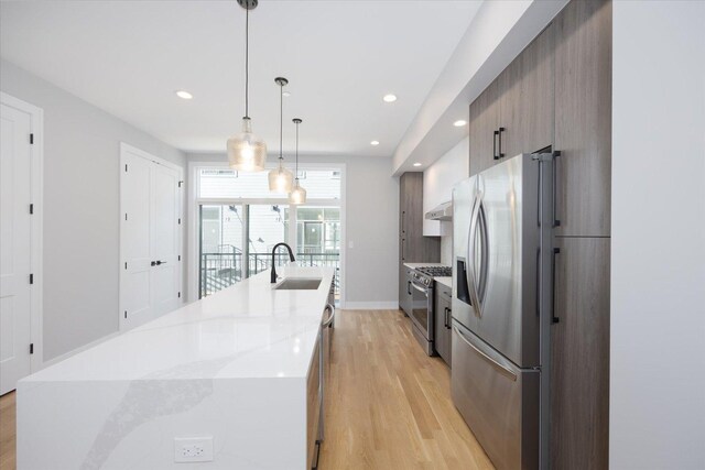 kitchen featuring hanging light fixtures, appliances with stainless steel finishes, sink, an island with sink, and light hardwood / wood-style floors