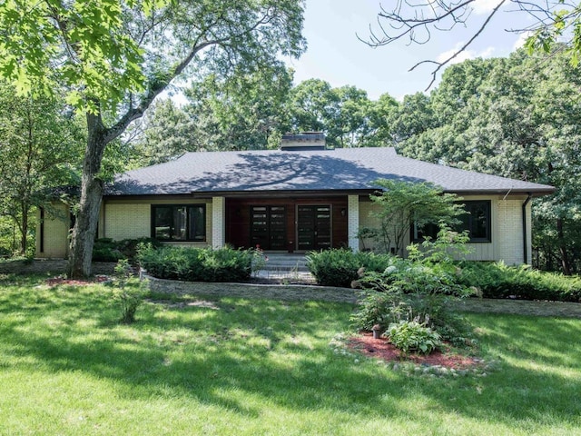 view of front facade featuring a shingled roof, brick siding, a chimney, and a front lawn