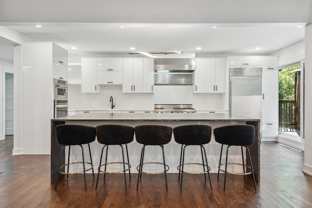 kitchen featuring tasteful backsplash, white cabinets, dark wood-type flooring, a kitchen island, and appliances with stainless steel finishes