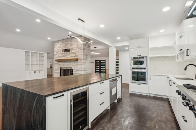 kitchen featuring a stone fireplace, sink, butcher block counters, beverage cooler, and double oven