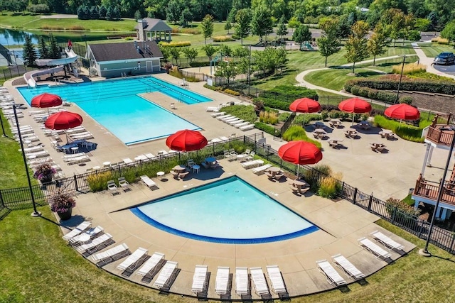 community pool featuring a water view, a patio area, fence, and a water slide