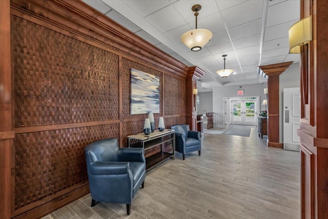 sitting room featuring french doors, light wood finished floors, a drop ceiling, and ornate columns