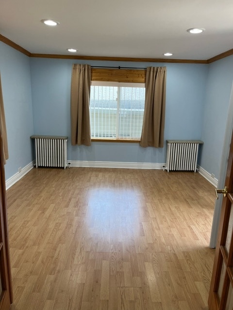 spare room featuring crown molding, light wood-type flooring, and radiator