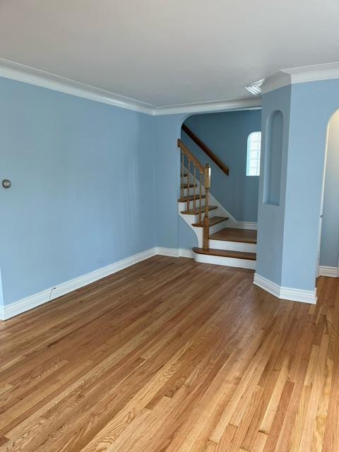 unfurnished room with arched walkways, light wood-type flooring, stairs, and ornamental molding