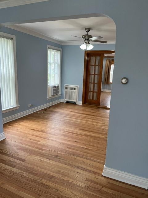 unfurnished room featuring radiator, wood finished floors, baseboards, arched walkways, and crown molding