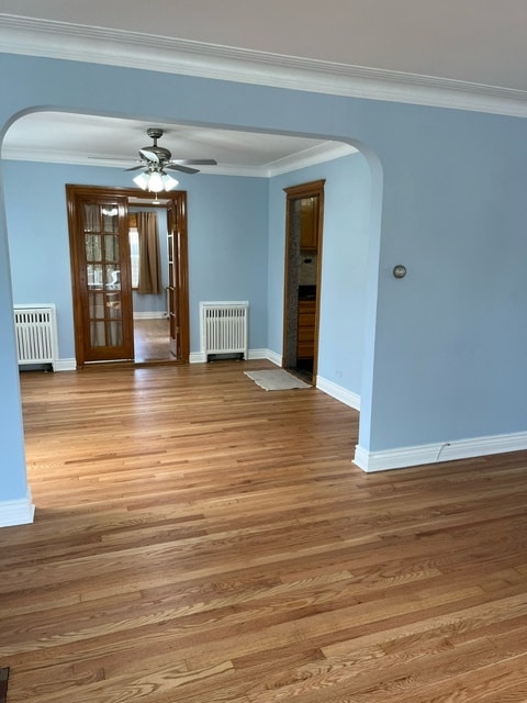 spare room featuring ceiling fan, wood-type flooring, crown molding, and radiator heating unit