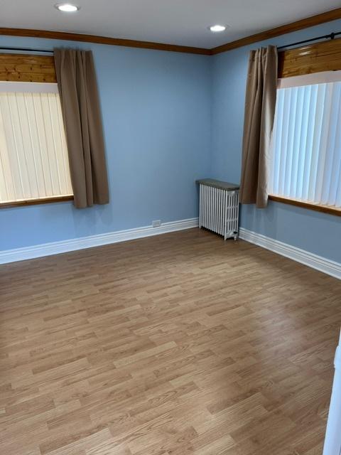 unfurnished room featuring wood finished floors, radiator heating unit, recessed lighting, crown molding, and baseboards