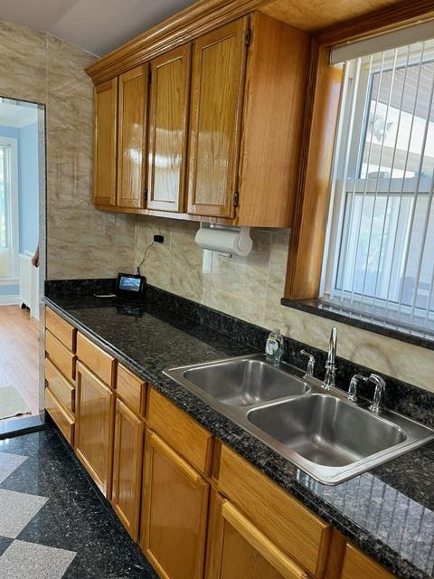 kitchen with brown cabinetry, backsplash, granite finish floor, and a sink