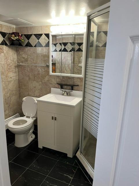 bathroom with vanity, a shower stall, toilet, and tile walls