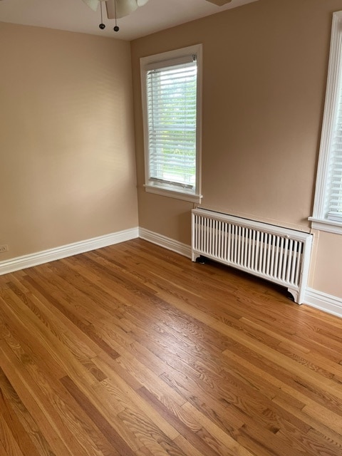 empty room featuring wood-type flooring, radiator, and ceiling fan