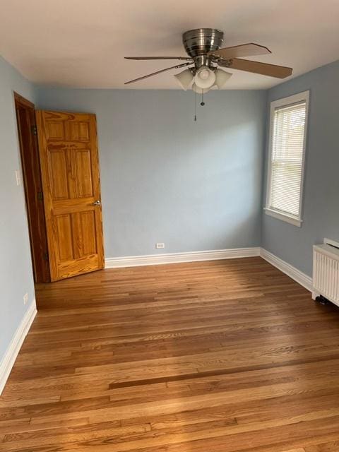 spare room featuring ceiling fan, baseboards, radiator heating unit, and light wood-style floors
