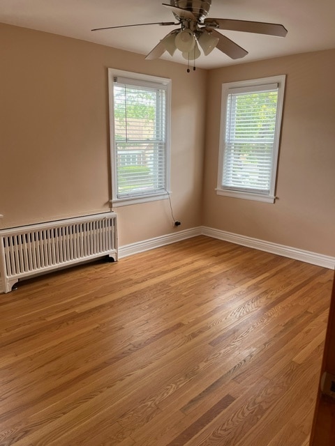 unfurnished room featuring radiator, a wealth of natural light, ceiling fan, and hardwood / wood-style floors