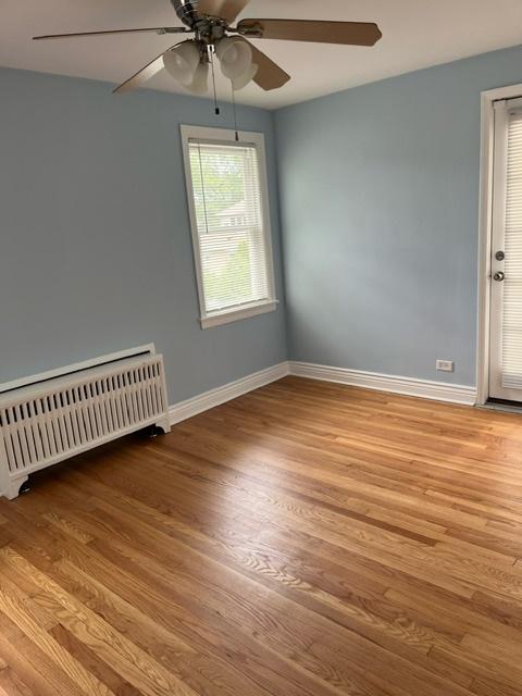 spare room featuring baseboards, a ceiling fan, radiator heating unit, and light wood finished floors