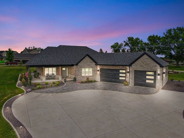 view of front of house featuring a shingled roof, concrete driveway, a lawn, a garage, and stone siding