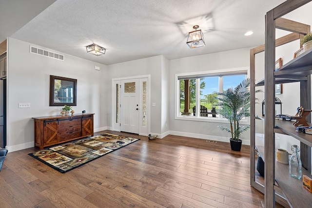 foyer entrance with baseboards, a textured ceiling, visible vents, and hardwood / wood-style floors