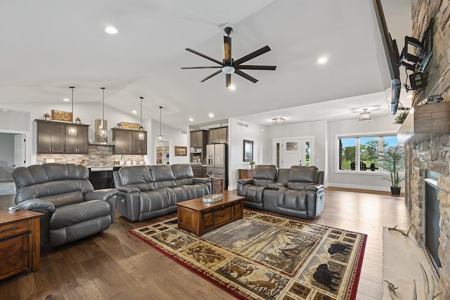 living room with lofted ceiling, a stone fireplace, hardwood / wood-style floors, and baseboards