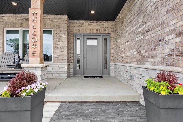 property entrance featuring covered porch, stone siding, and brick siding