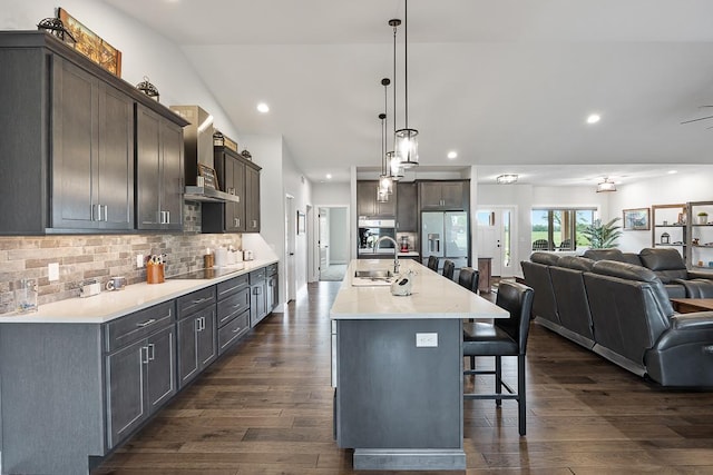 kitchen with lofted ceiling, open floor plan, dark wood-style flooring, a kitchen breakfast bar, and a sink