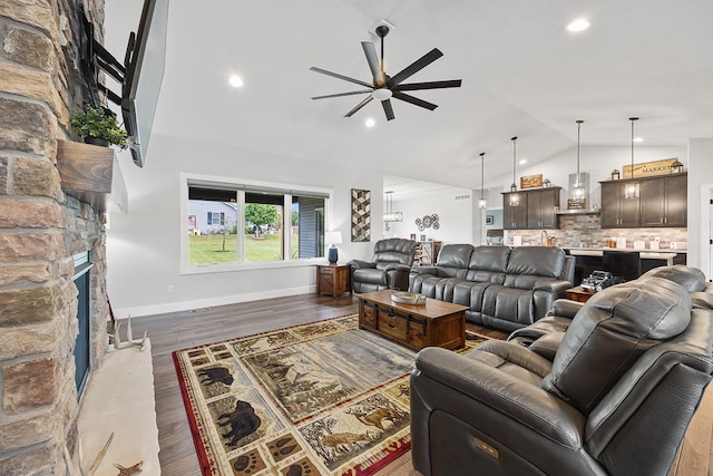 living room featuring baseboards, ceiling fan, dark wood-type flooring, a stone fireplace, and high vaulted ceiling