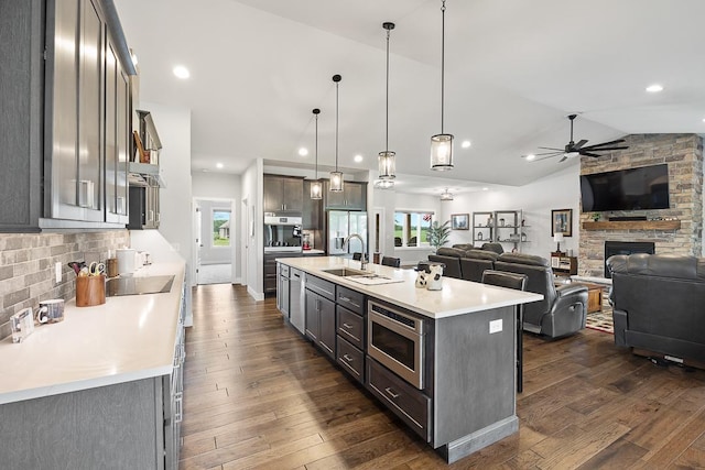 kitchen with a sink, vaulted ceiling, light countertops, appliances with stainless steel finishes, and dark wood-style floors