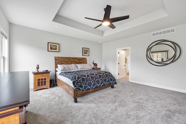 carpeted bedroom featuring a ceiling fan, visible vents, a tray ceiling, and baseboards