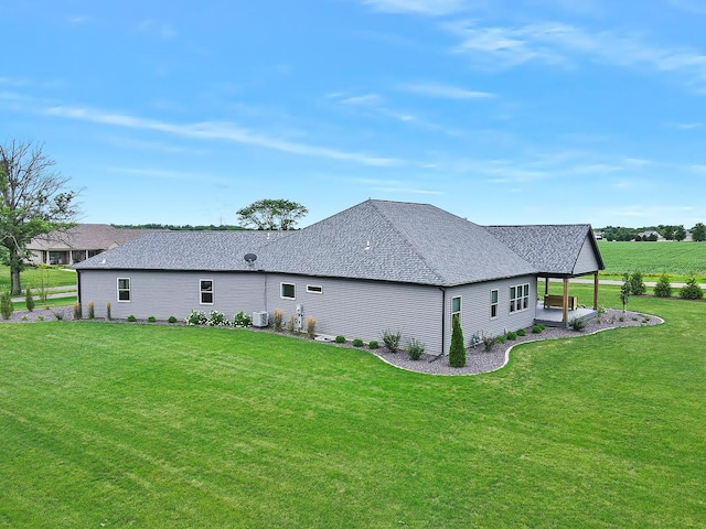 rear view of house featuring roof with shingles, central AC, and a yard