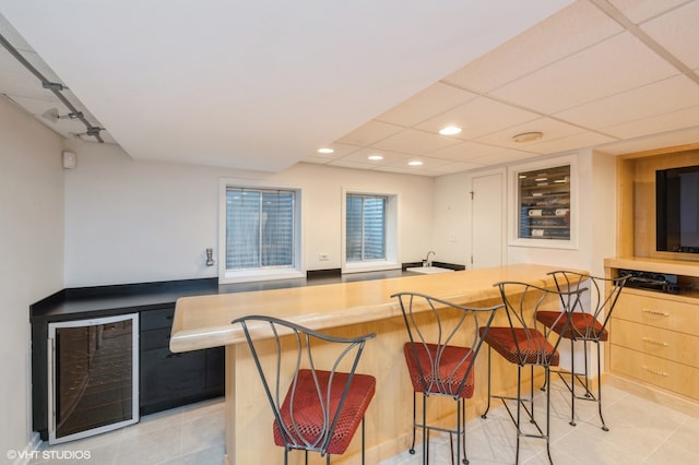 bar with a drop ceiling, light tile patterned flooring, and beverage cooler