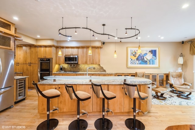 kitchen with appliances with stainless steel finishes, decorative light fixtures, light wood-type flooring, and beverage cooler