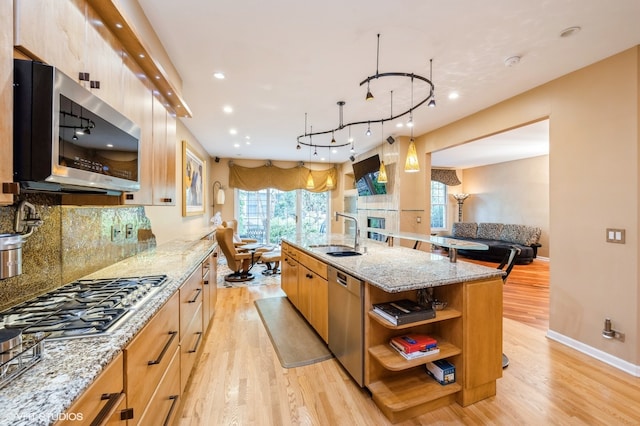 kitchen with light wood-type flooring, sink, appliances with stainless steel finishes, and a center island with sink