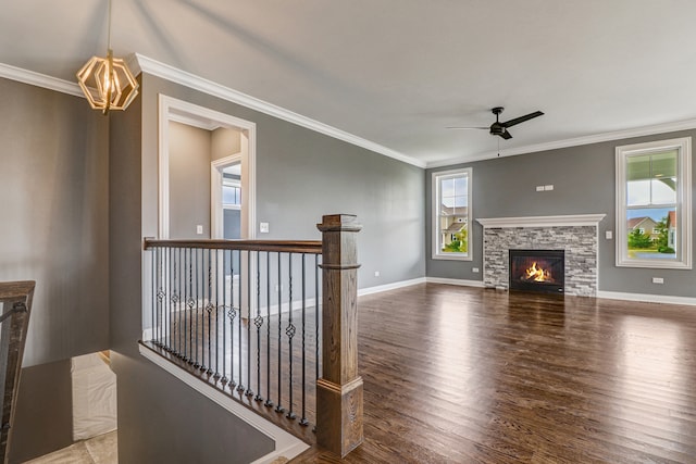 unfurnished living room featuring a fireplace, crown molding, ceiling fan with notable chandelier, and hardwood / wood-style floors