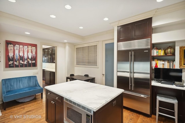 kitchen featuring ornamental molding, built in appliances, light hardwood / wood-style floors, and a center island