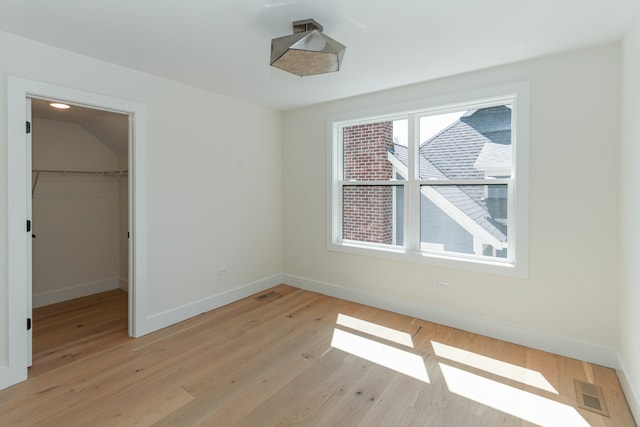 unfurnished bedroom featuring multiple windows, a walk in closet, light hardwood / wood-style flooring, and a closet