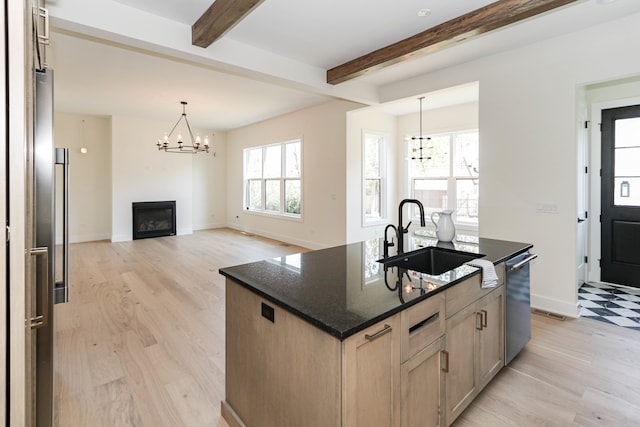 kitchen featuring sink, light hardwood / wood-style flooring, beam ceiling, and an island with sink