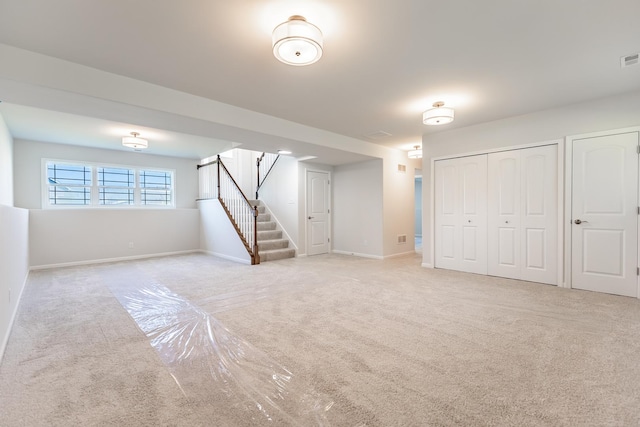 below grade area featuring light carpet, baseboards, visible vents, and stairway