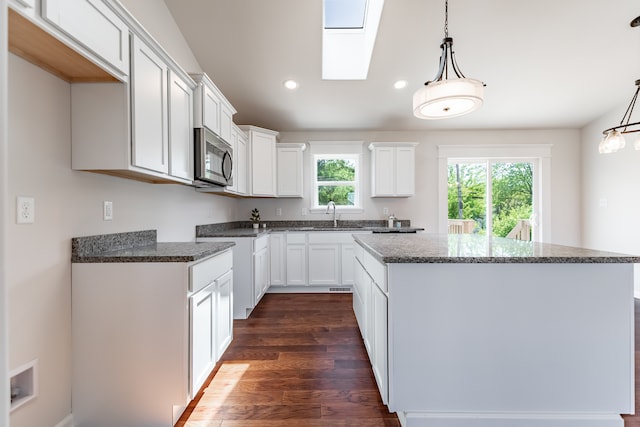 kitchen with pendant lighting, dark wood-type flooring, a kitchen island, white cabinets, and a skylight