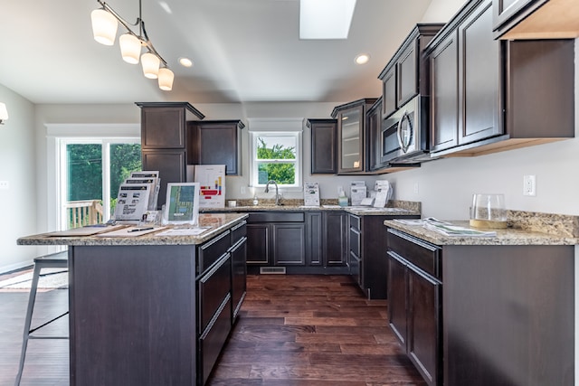 kitchen featuring light stone counters, pendant lighting, dark wood-style flooring, stainless steel microwave, and a kitchen breakfast bar