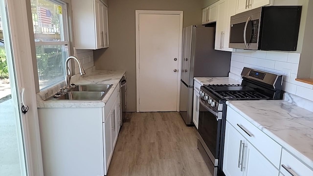 kitchen with white cabinets, light wood-type flooring, sink, backsplash, and stainless steel appliances