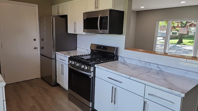 kitchen with appliances with stainless steel finishes, backsplash, white cabinets, light stone countertops, and light hardwood / wood-style floors