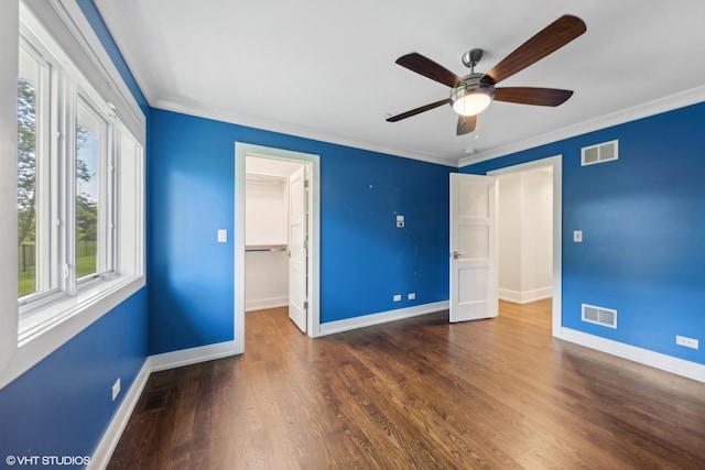 unfurnished bedroom featuring a spacious closet, ceiling fan, a closet, dark wood-type flooring, and crown molding